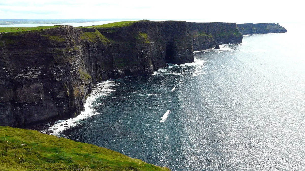 The Cliffs of Moher, tall dark sea cliffs running along the Atlantic coast under a bright sky