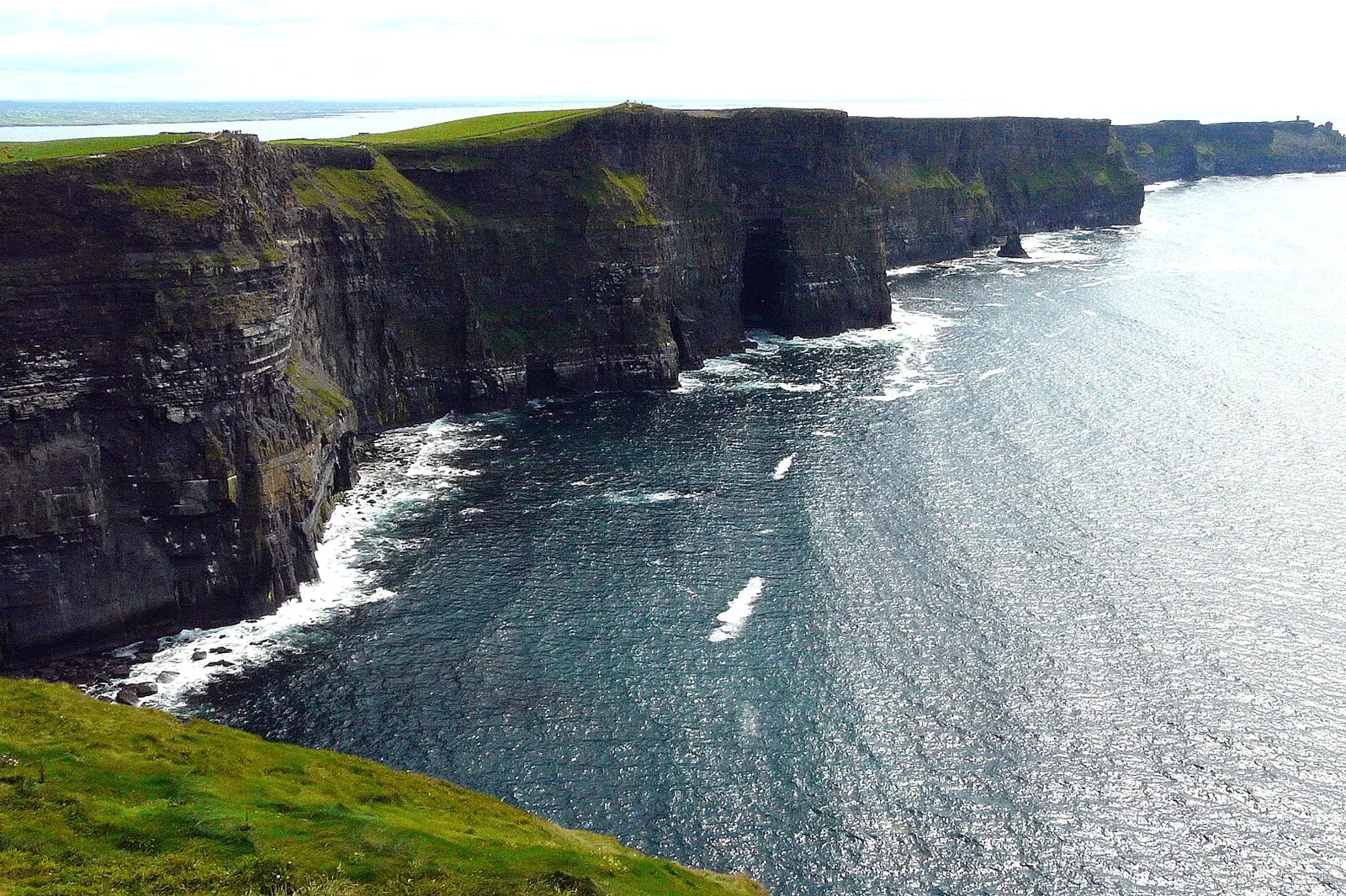 The Cliffs of Moher in County Clare, tall dark sea cliffs running along the Atlantic coast under a bright sky